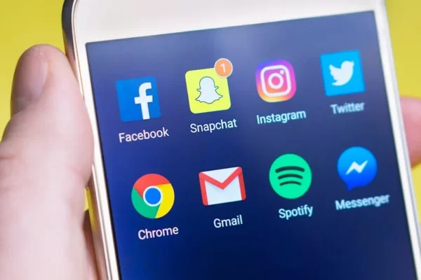 A person's hand holding a smartphone displaying social media and communication apps.