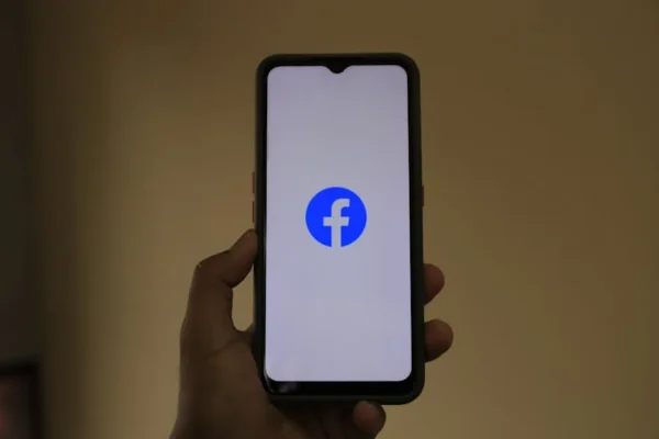 A smartphone held in hand showing the Facebook logo on its screen.