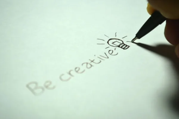 Close-up of handwritten 'Be creative' with a light bulb sketch on paper.