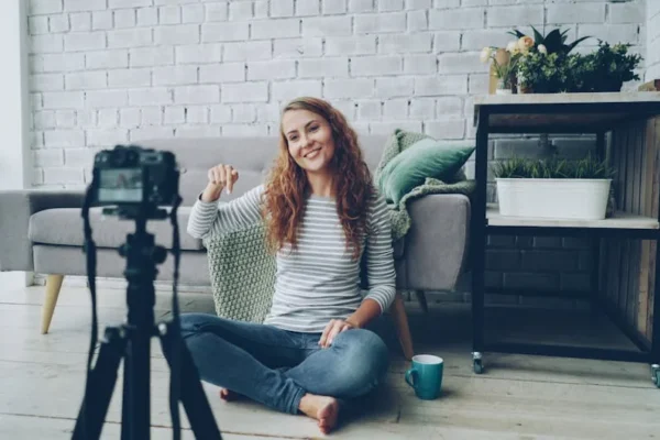Smiling woman sitting on floor, recording video in cozy room.
