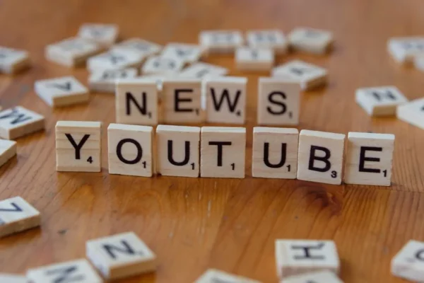 Scrabble tiles spelling words on wooden surface, focusing on YouTube and News.