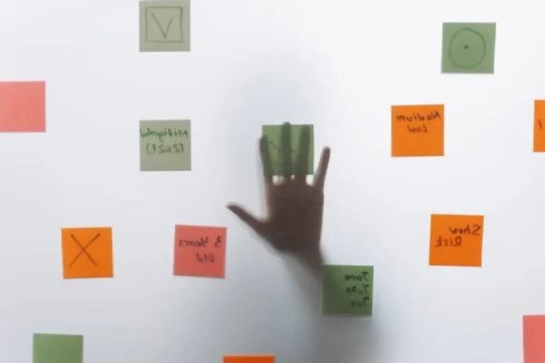 A hand reaching behind glass covered with colorful sticky notes, symbolizing brainstorming and ideas.