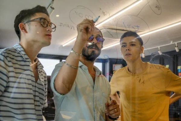 Young professionals brainstorming and writing ideas on a transparent board in an office setting.