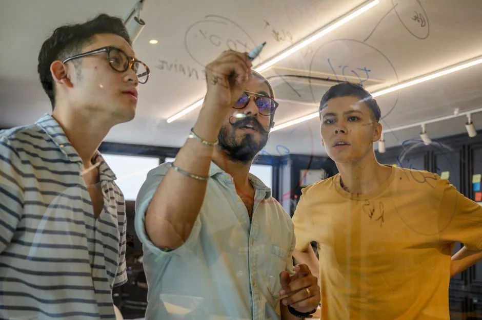 Young professionals brainstorming and writing ideas on a transparent board in an office setting.