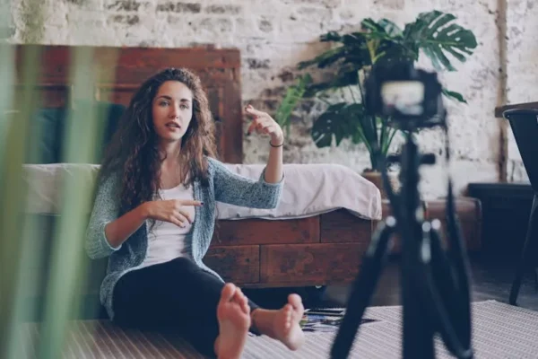 Woman sitting on floor filming vlog, discussing engaging topic. Home setting with cozy atmosphere.