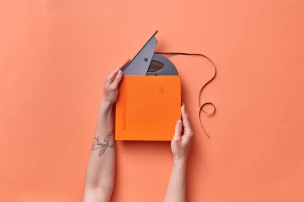A pair of hands holding a vintage film tape in an orange box against a matching orange background.