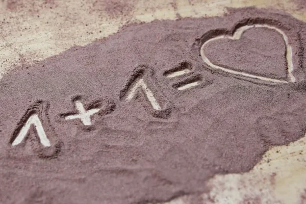 Equation written in sand with 1+1 equals heart. Expresses love and creativity.
