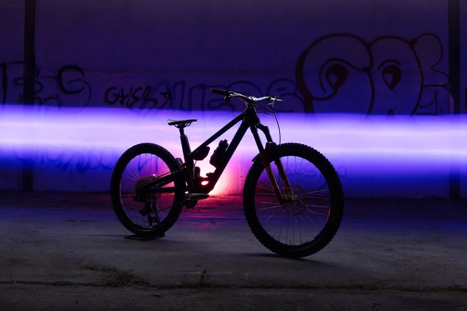 A mountain bike silhouette with vibrant light trails in an urban setting at night.