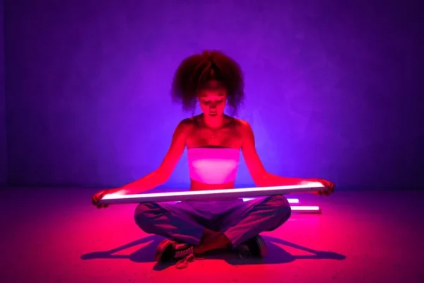 A woman in a studio, illuminated by neon lights, holds a glowing tube, creating a vibrant and modern scene.